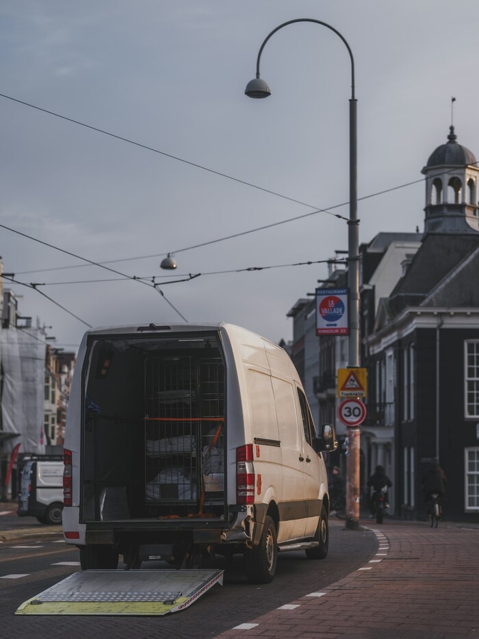 White delivery van with open back and ramp on a city street