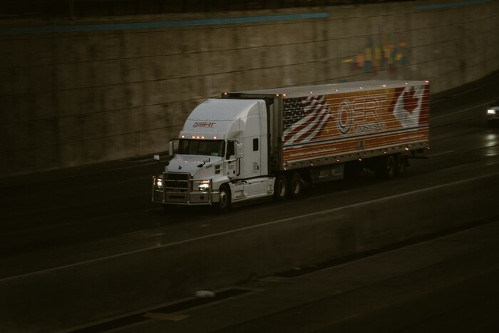 Semi-truck driving along a highway beside a concrete wall